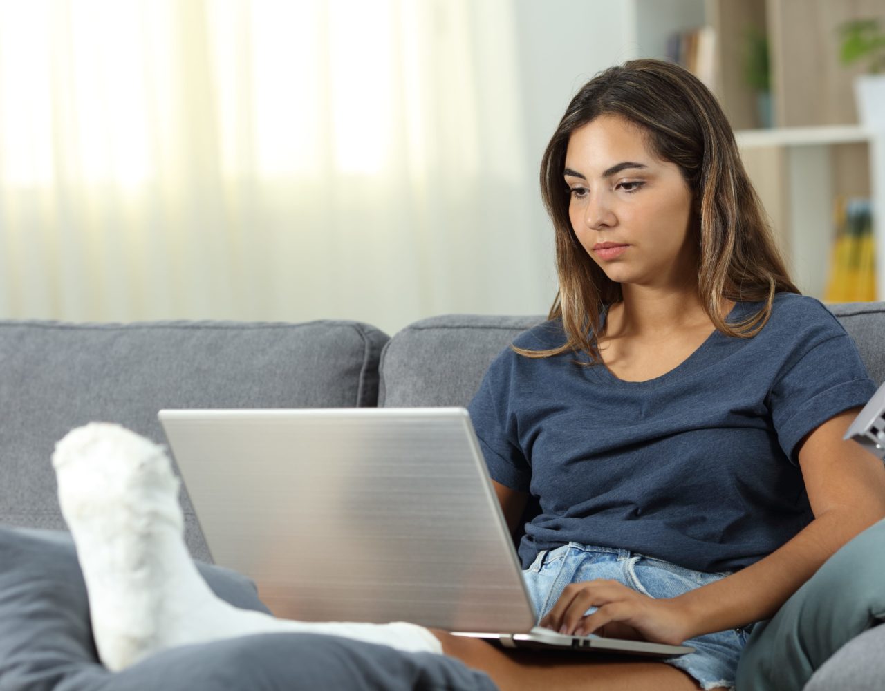 A women with a fractured leg using laptop on her couch