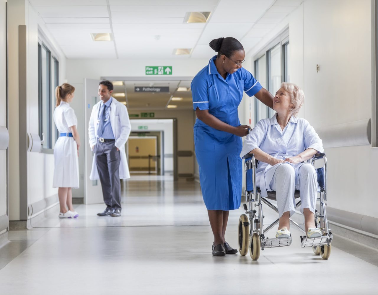 A female nurse with a patient on a wheel chair while two health professionals are in a conversation