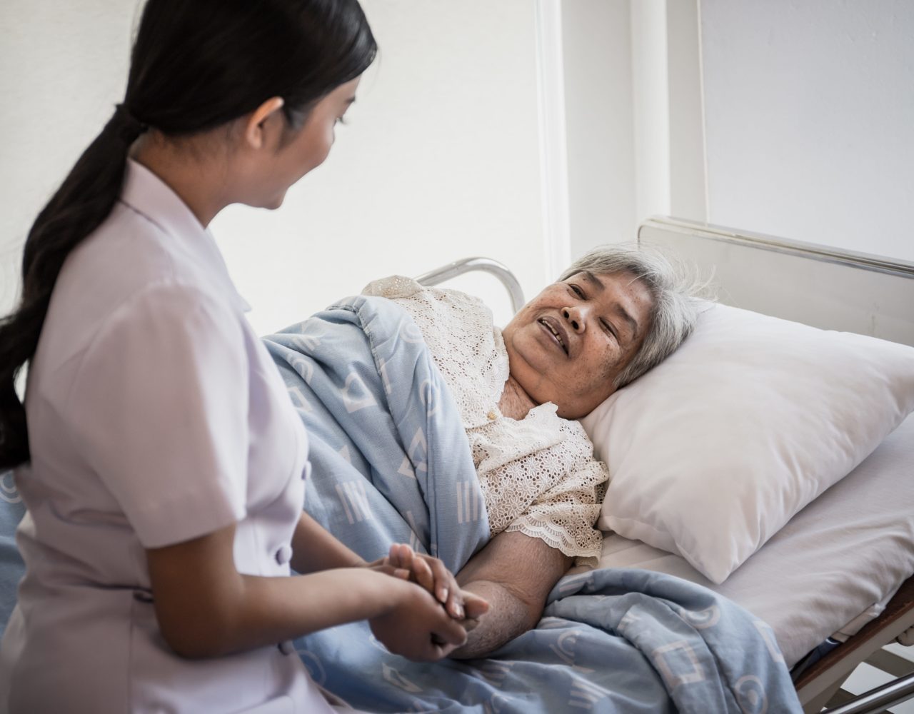 A female healthcare professional with an old lady patient laying on bed