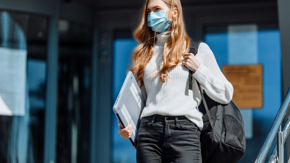 Beautiful young girl in a mask from coronovirus, student on the background of educational envy, women returning from work, remote work, covid-19, against the background of a glass business building