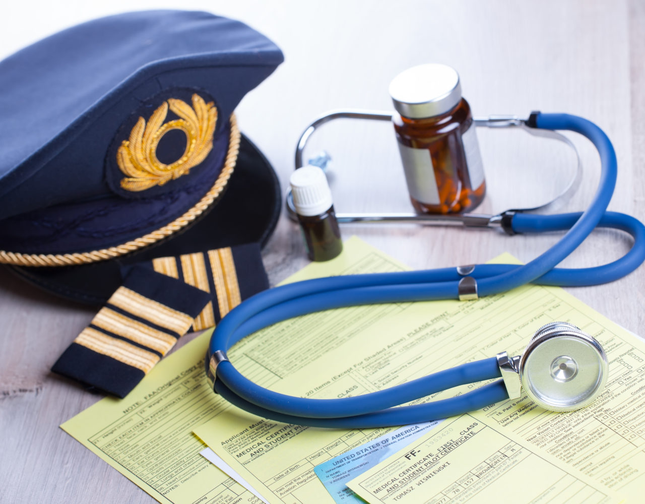 Close up of an airplane pilot equipment hat and epaluetes with doctor's stethoscope, forms, medical and pilot certificate and drugs. Conceptual image of medical exam
